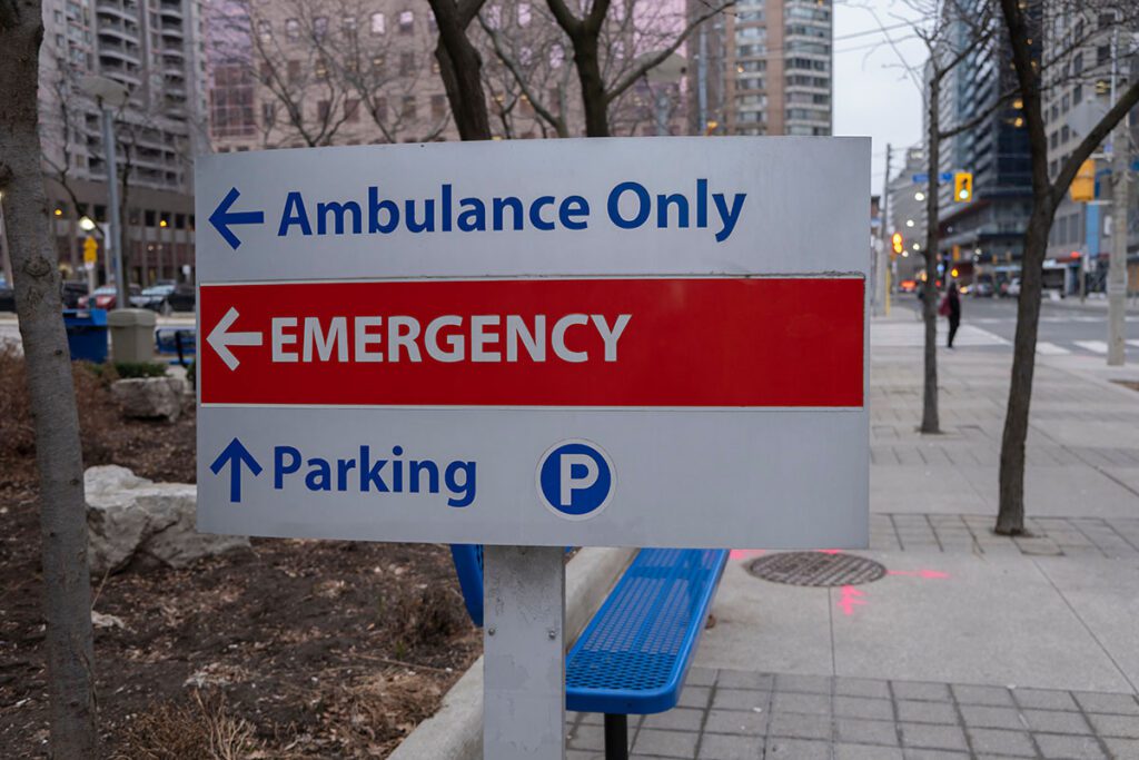 A hospital sign reads "Ambulance Only," "Emergency," and "Parking."