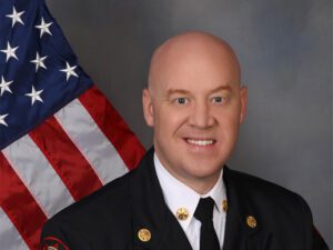 A headshot of a man in uniform sitting in front of an American flag.